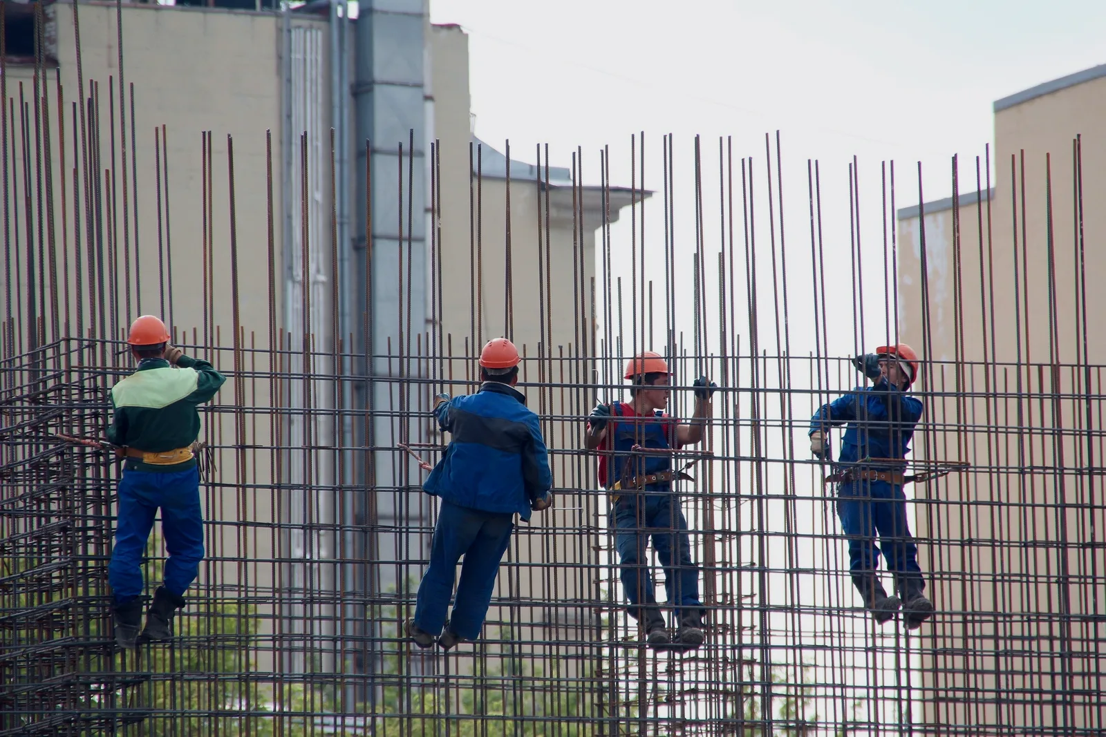 Four construction workers in orange helmets working on a steel reinforcement structure