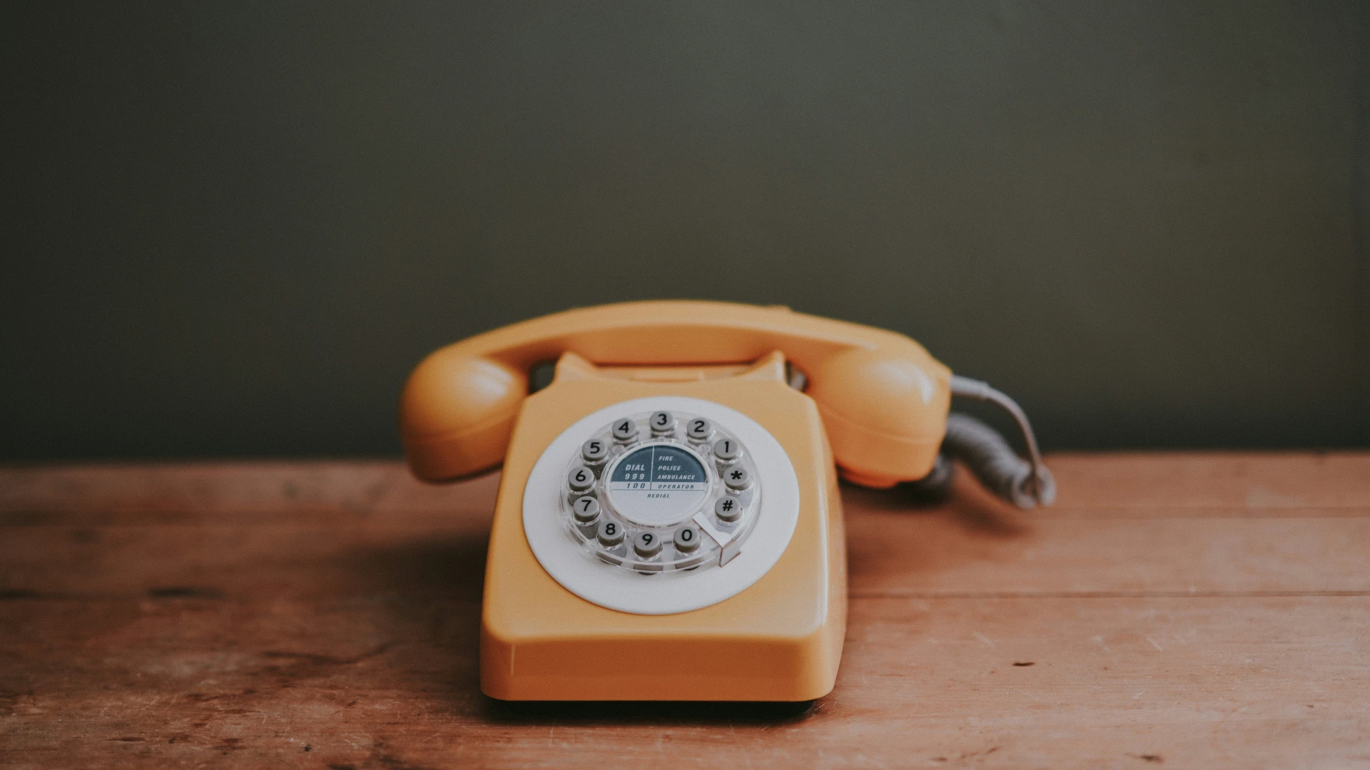 Orangefarbenes Wählscheibentelefon auf einem Holztisch als Sinnbild für eine einheitliche Telefonnummer im Netz