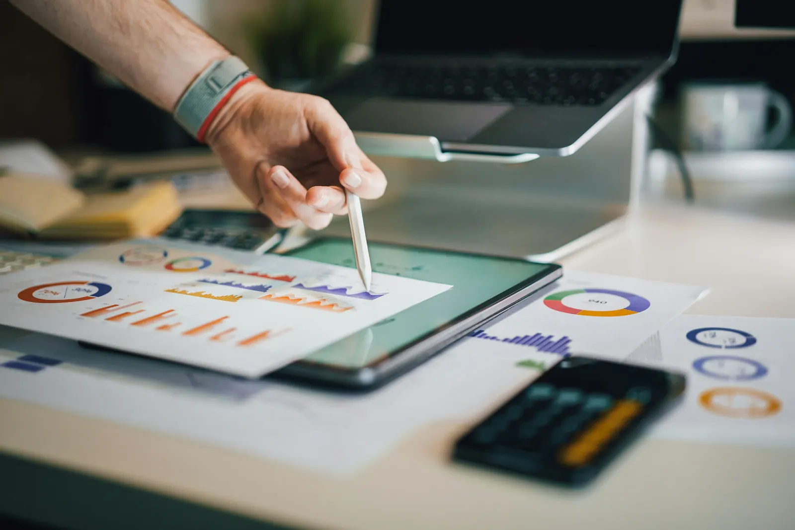 Hand mit Stift analysiert Preis- und Kosten-Diagramme am Laptop-Arbeitsplatz
